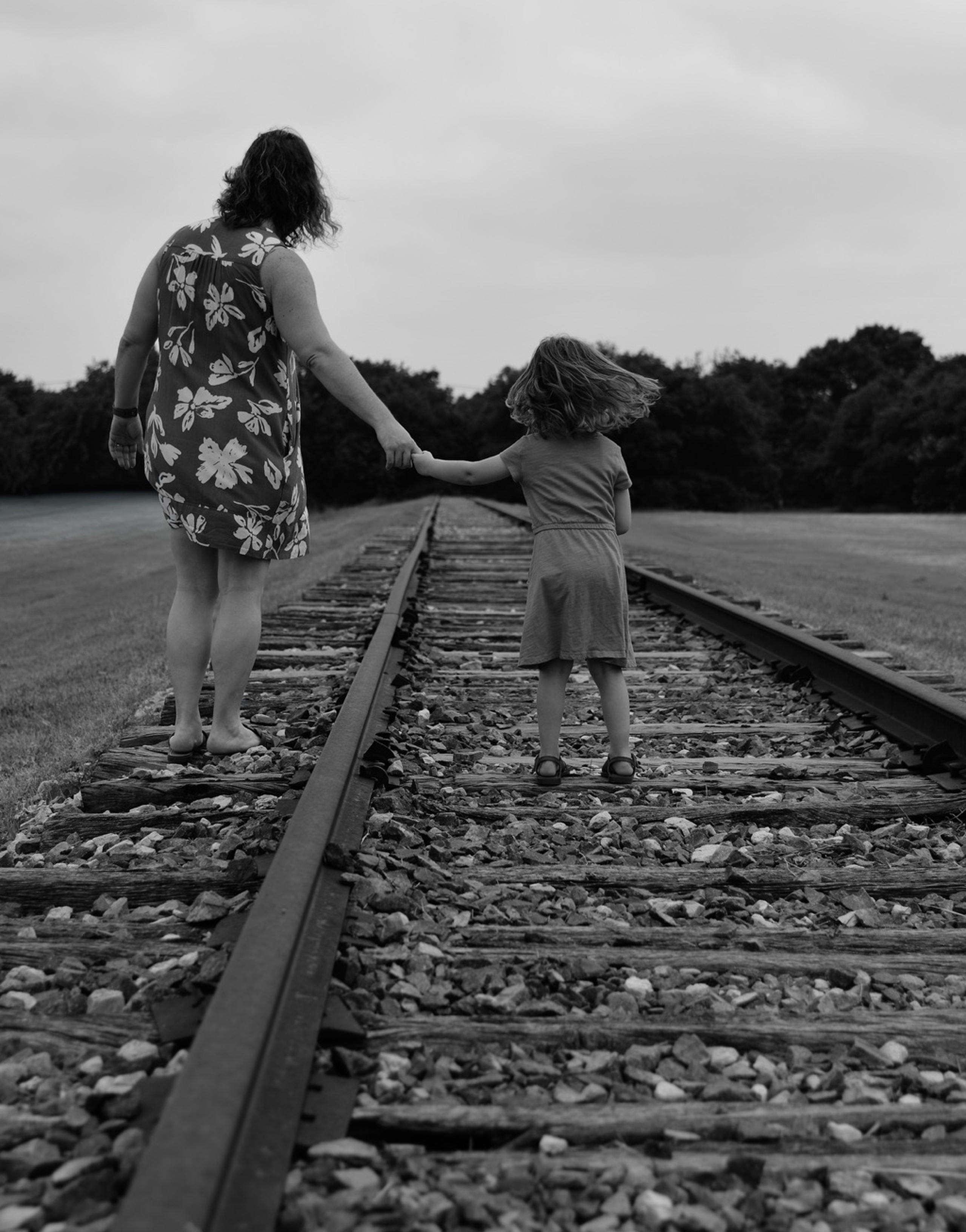 black and white image of an adult and child walking on an old, out of service, train track